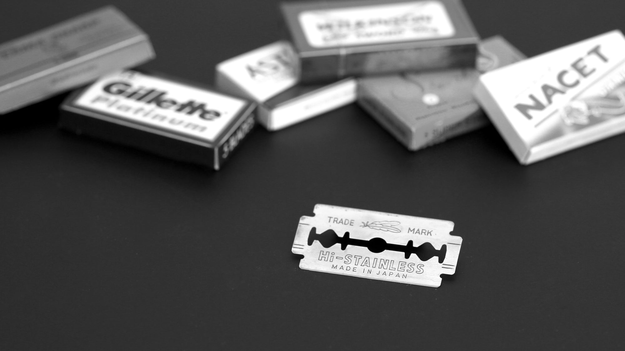 A razor blade on a black background with packs of other brands blurred behind