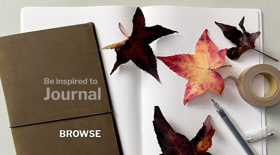 Be inspired to journal leather journal cover on top of open dot journal pages with a pen and bright autumn leaves scattered