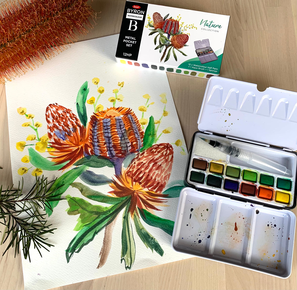 Artistic depiction of flowers with a watercolor set and paint box on a wooden surface.