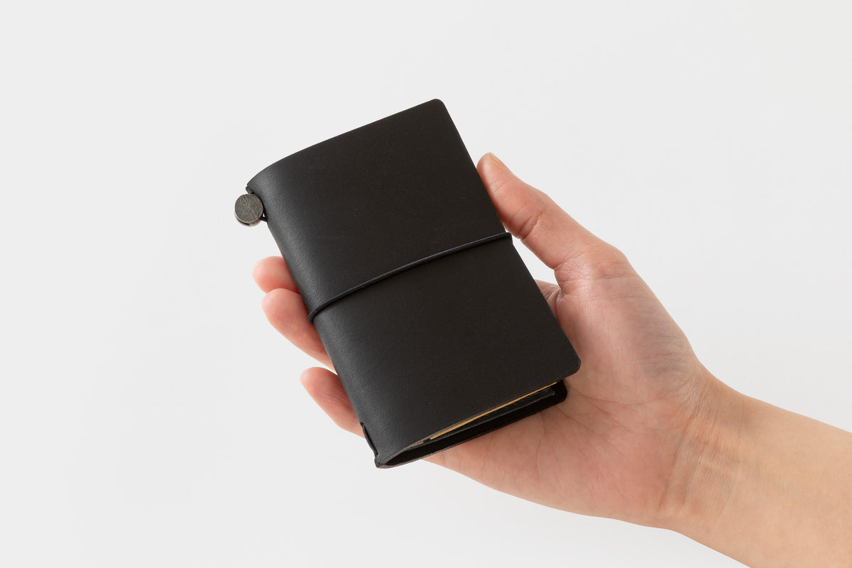 Hand holding a black leather notebook against a white background