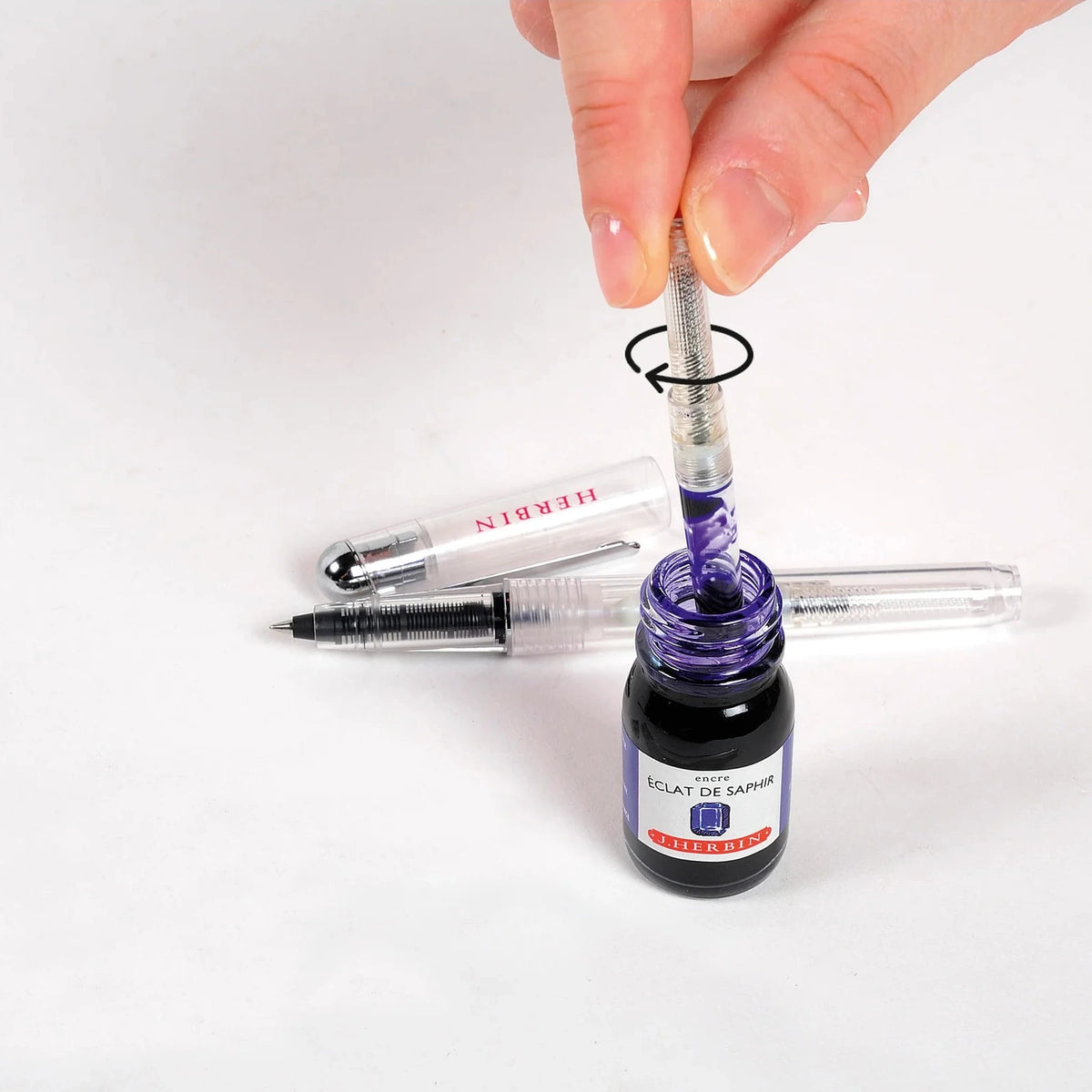 Person filling a pen with purple ink from a bottle on a white background