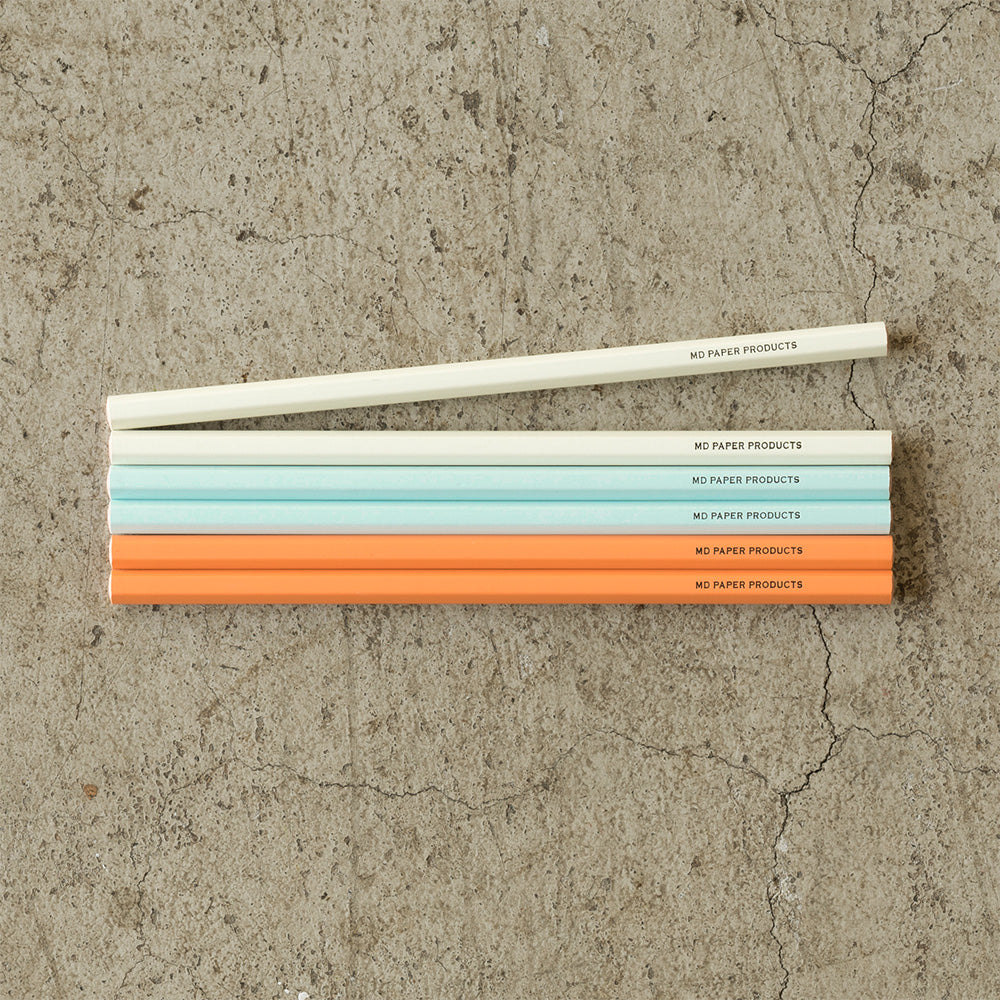 A set of six MD Midori color pencils in gray, light blue, and orange, packaged in a sleek, beige box with Japanese text.