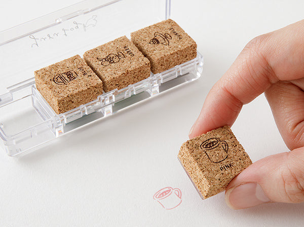 Cork stamp set with a hand holding a stamp and a clear holder on a white background.