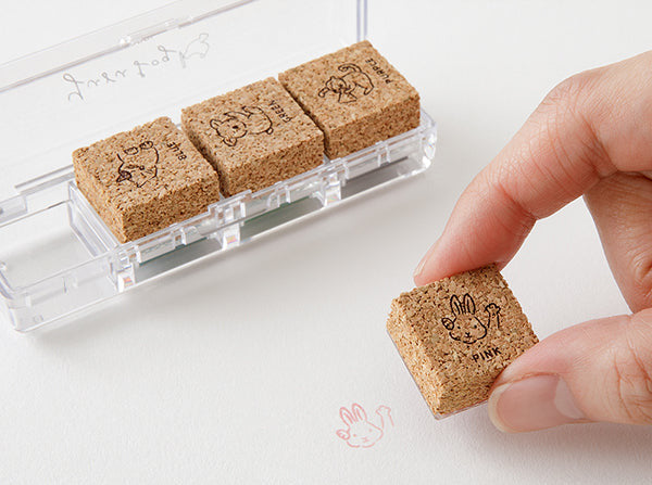 Cork stamp set with a hand holding a stamp and a clear holder on a white background.