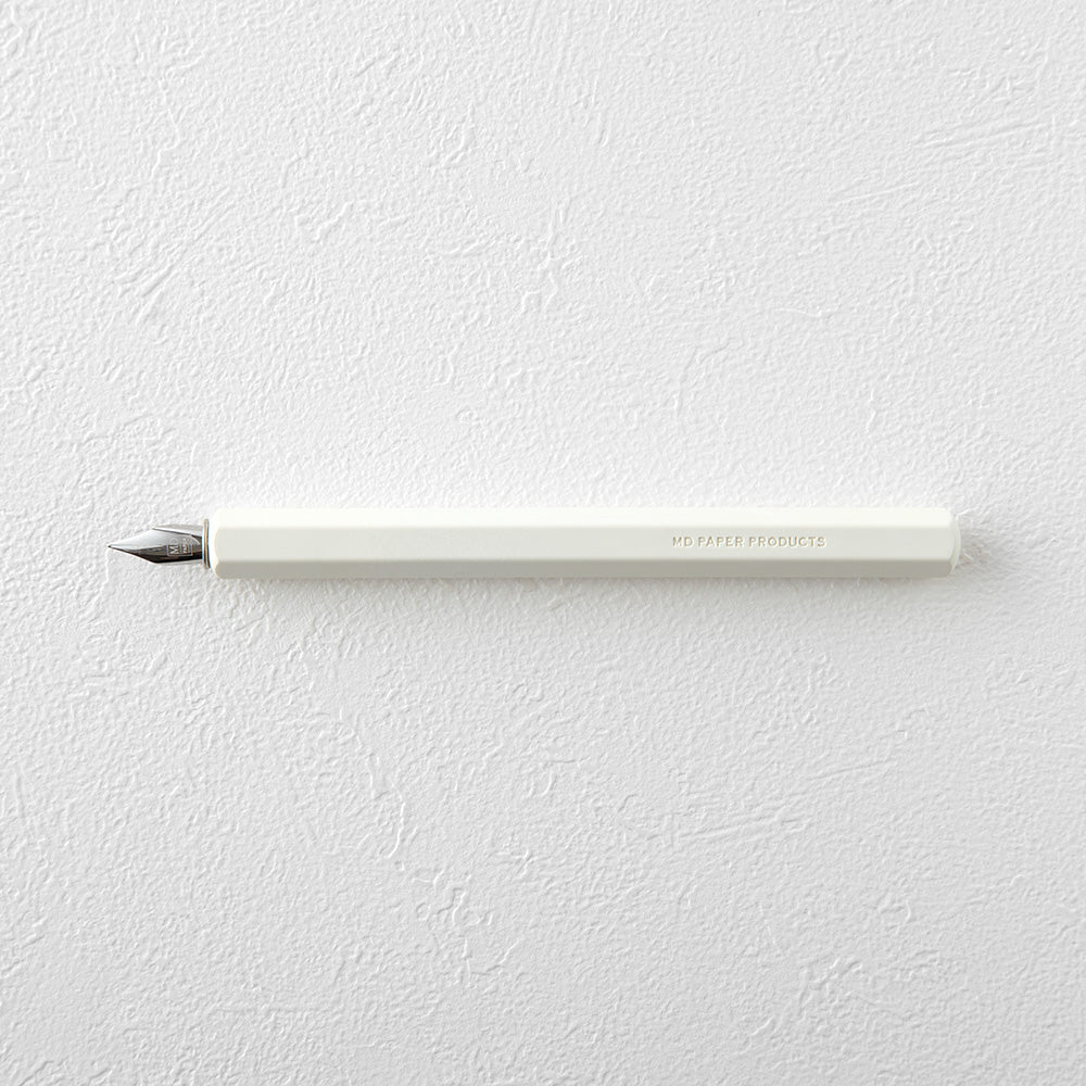 The white MD paper dip pen with hexagonal grip and chrome nib, seen from the top on a textured white surface