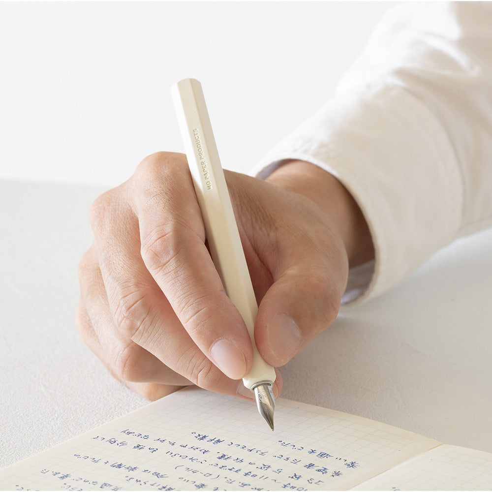 The dip pen in use, held by a male hand above a page of Japanese characters