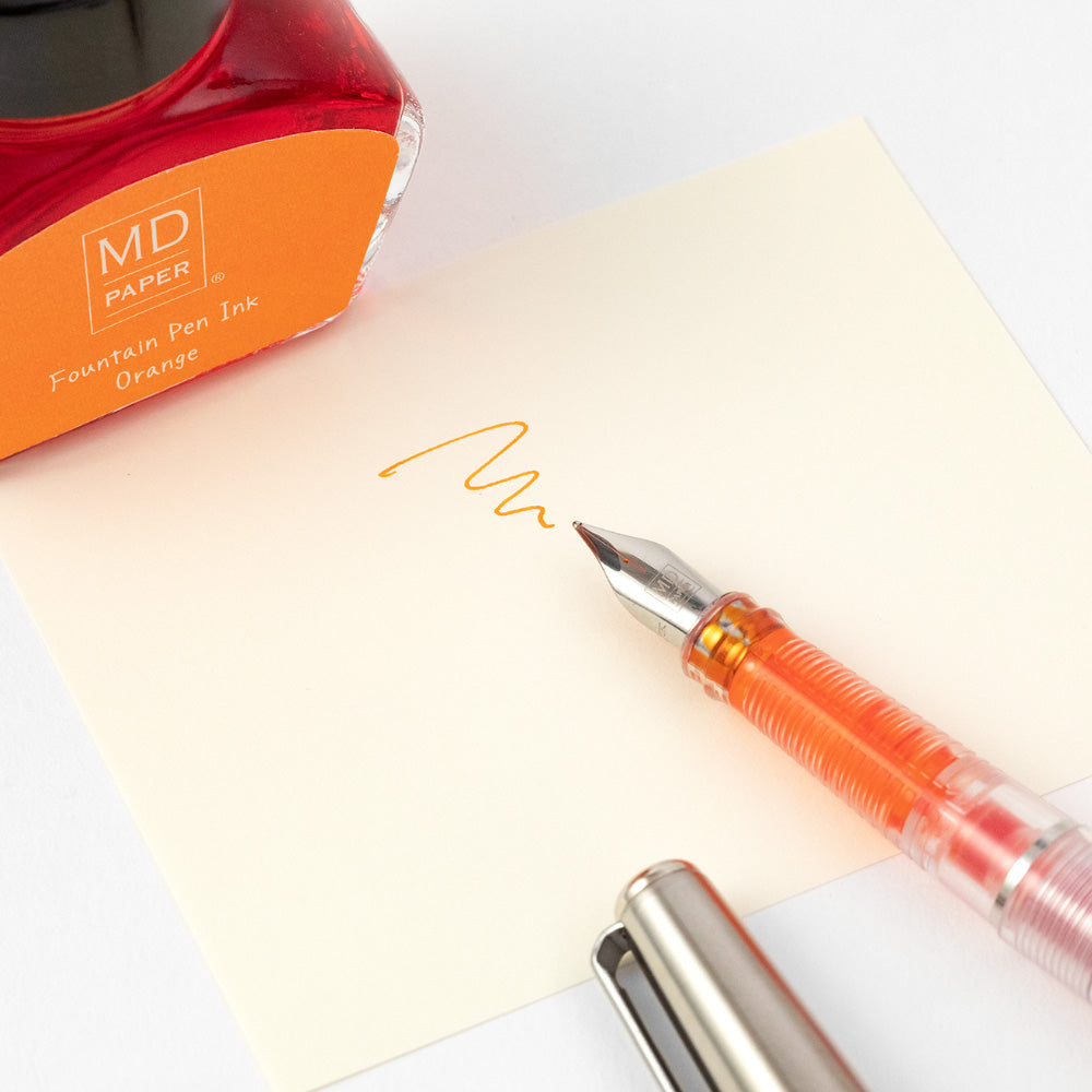 Detail of orange bottle of ink and a line drawn in orange ink with a fountain pen which is also partially in shot