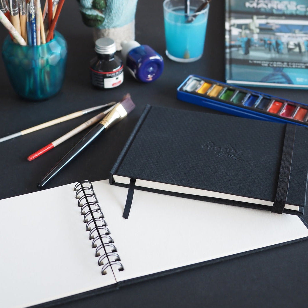 Art supplies including brushes, paint, and a notebook on a table.