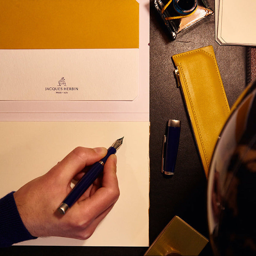 Hand writing on a Jaeger-LeCoultre notebook with fountain pen and inkwell on a dark surface