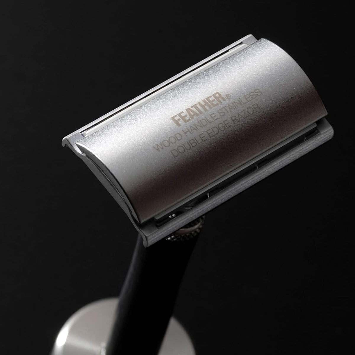 Silver safety razor with 'Feather' branding on a black background