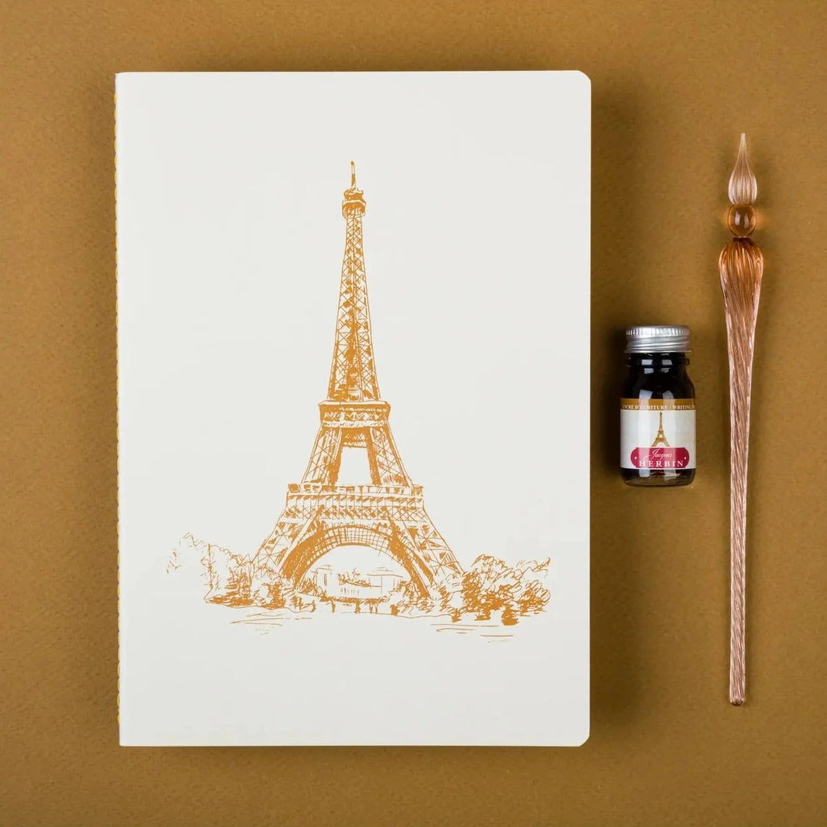 Notebook with Eiffel Tower design, ink bottle, and brush on a brown background