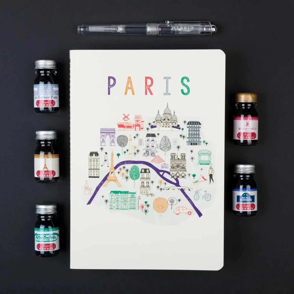 Notebook with Paris illustration surrounded by ink bottles on a dark background