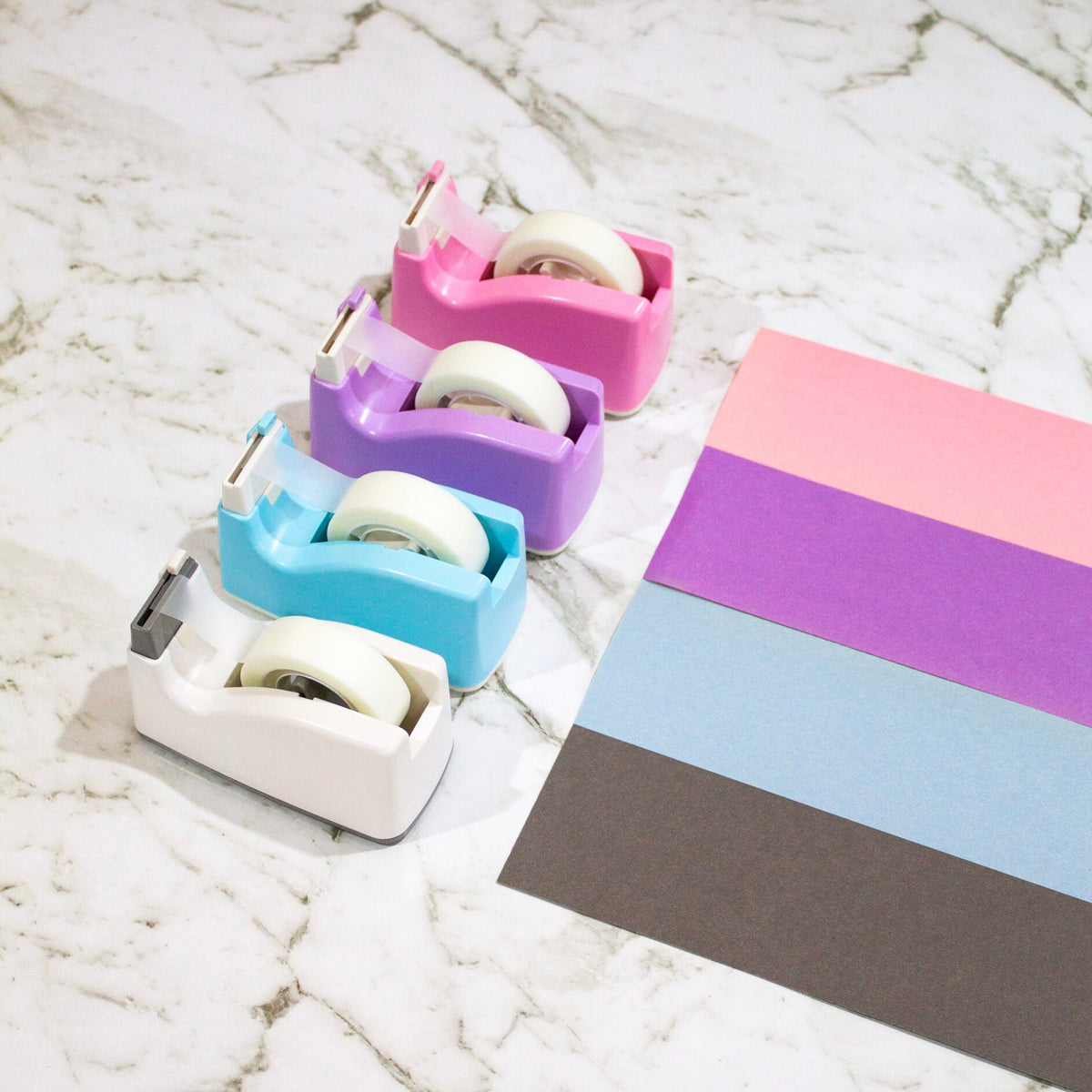 Set of colorful tape dispensers with matching rolls on a marble surface
