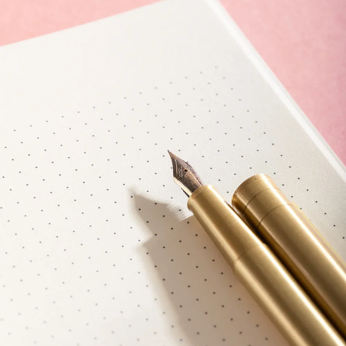 Gold fountain pen on a white notebook with a pink background