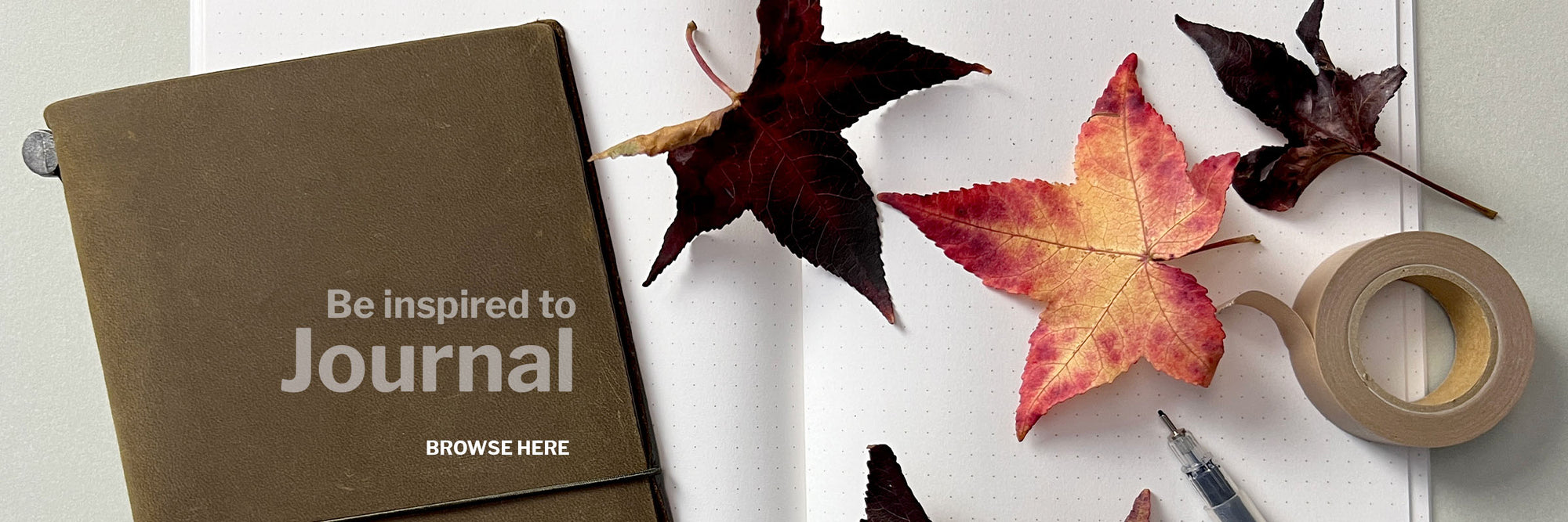 Be inspired to journal leather journal cover on top of open dot journal pages with a pen and bright autumn leaves scattered