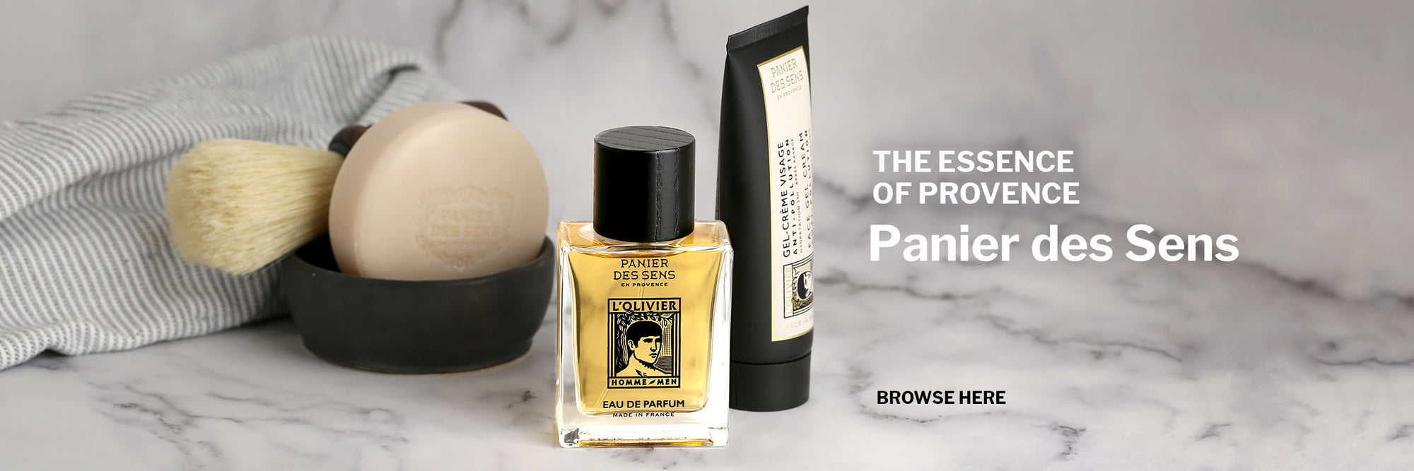 Shavibg soap and brush with black terracotta bowl, Eau de Parfum bottle in centre, and Face Gel Cream on a white and grey marble background with grey and white striped face cloth