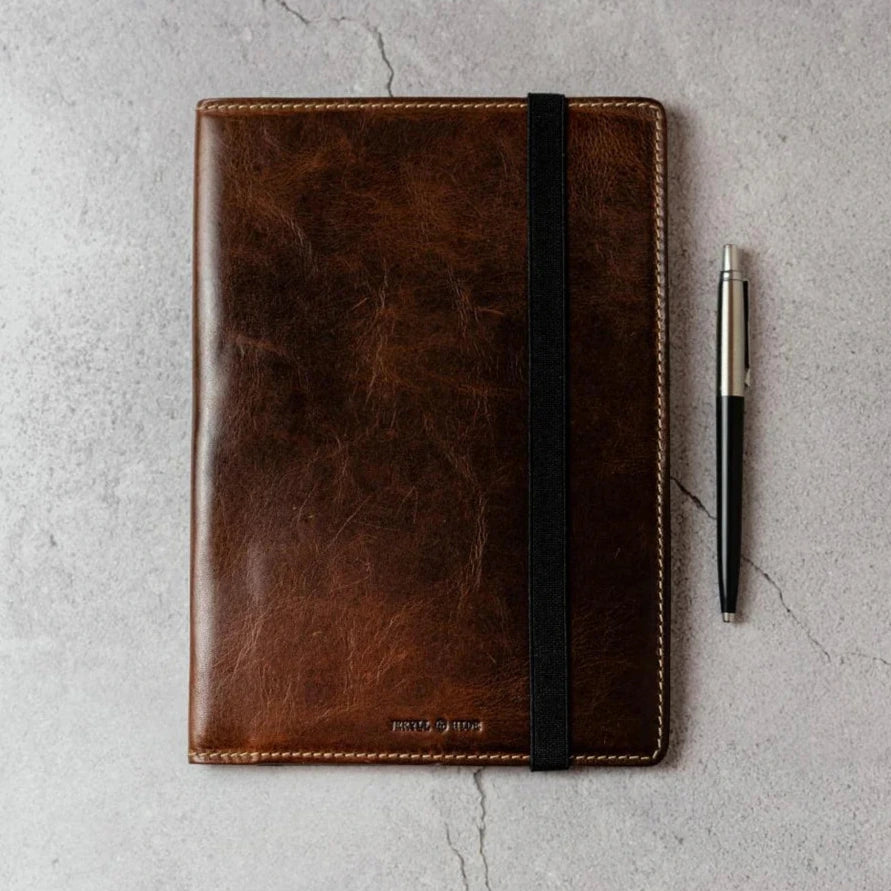 Brown leather notebook with a pen on a gray surface