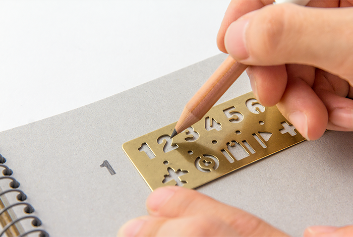 Person using a brass ruler with numbers and symbols on a notebook page.