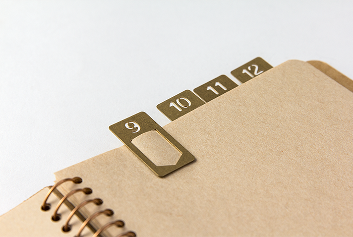 Beige notebook with gold metal tab markers on a light gray background