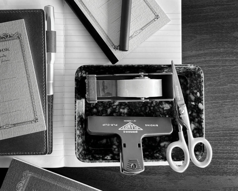 Desk setup with office supplies including a pen, scissors, and a tape dispenser on a wooden surface.