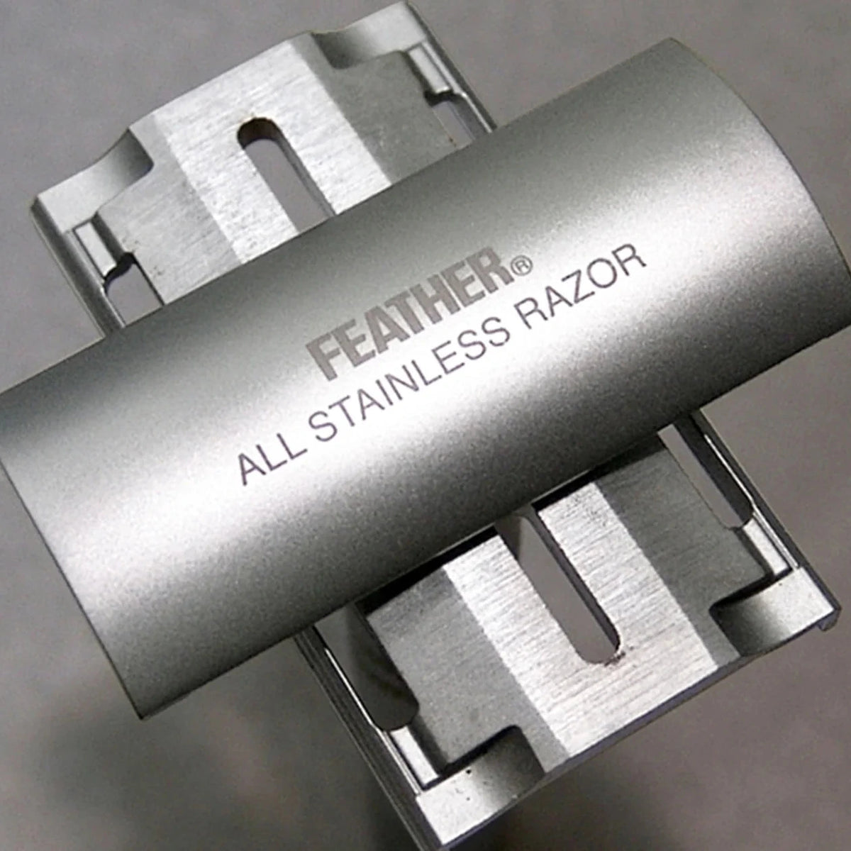 Metallic all-stainless razor with 'Feather' branding on a gray background