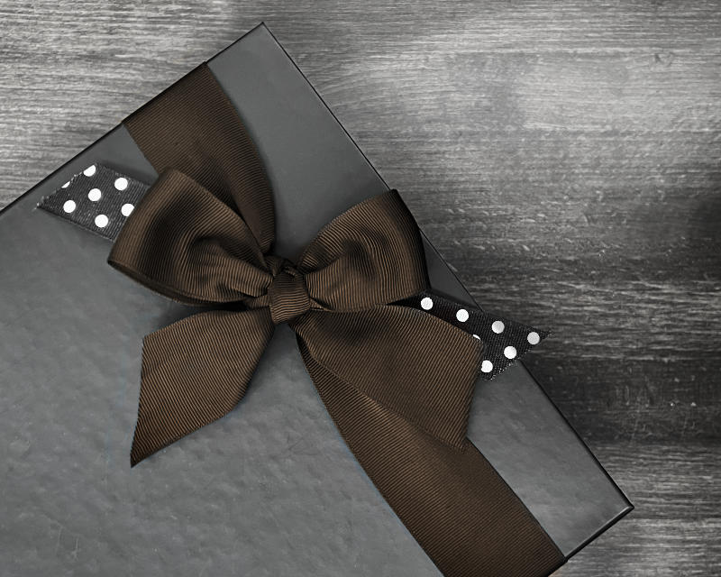 Black gift box with a brown ribbon and decorative elements on a gray surface