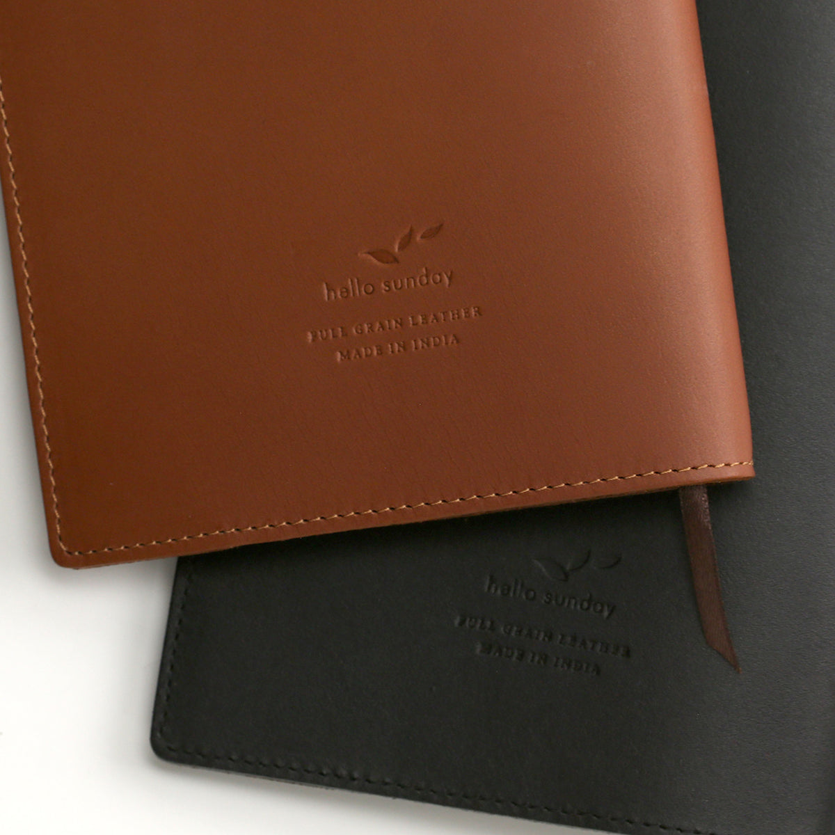 Hello Sunday logo on the back of one tan and one black leather jacket for notebooks