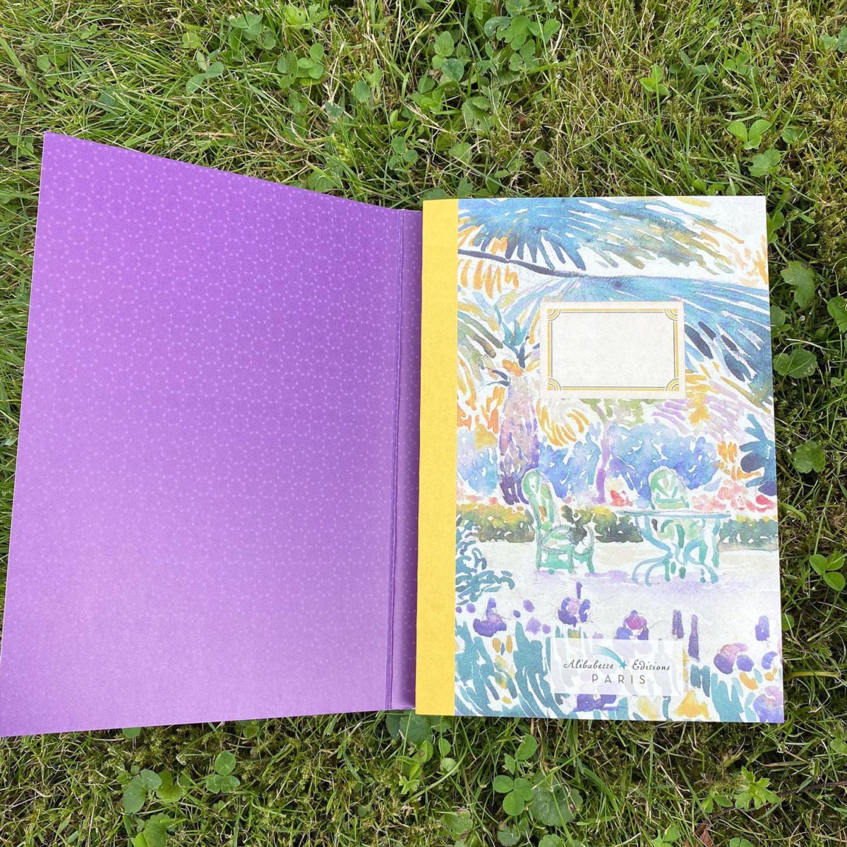 Open notebook with purple interior and colorful exterior on grass