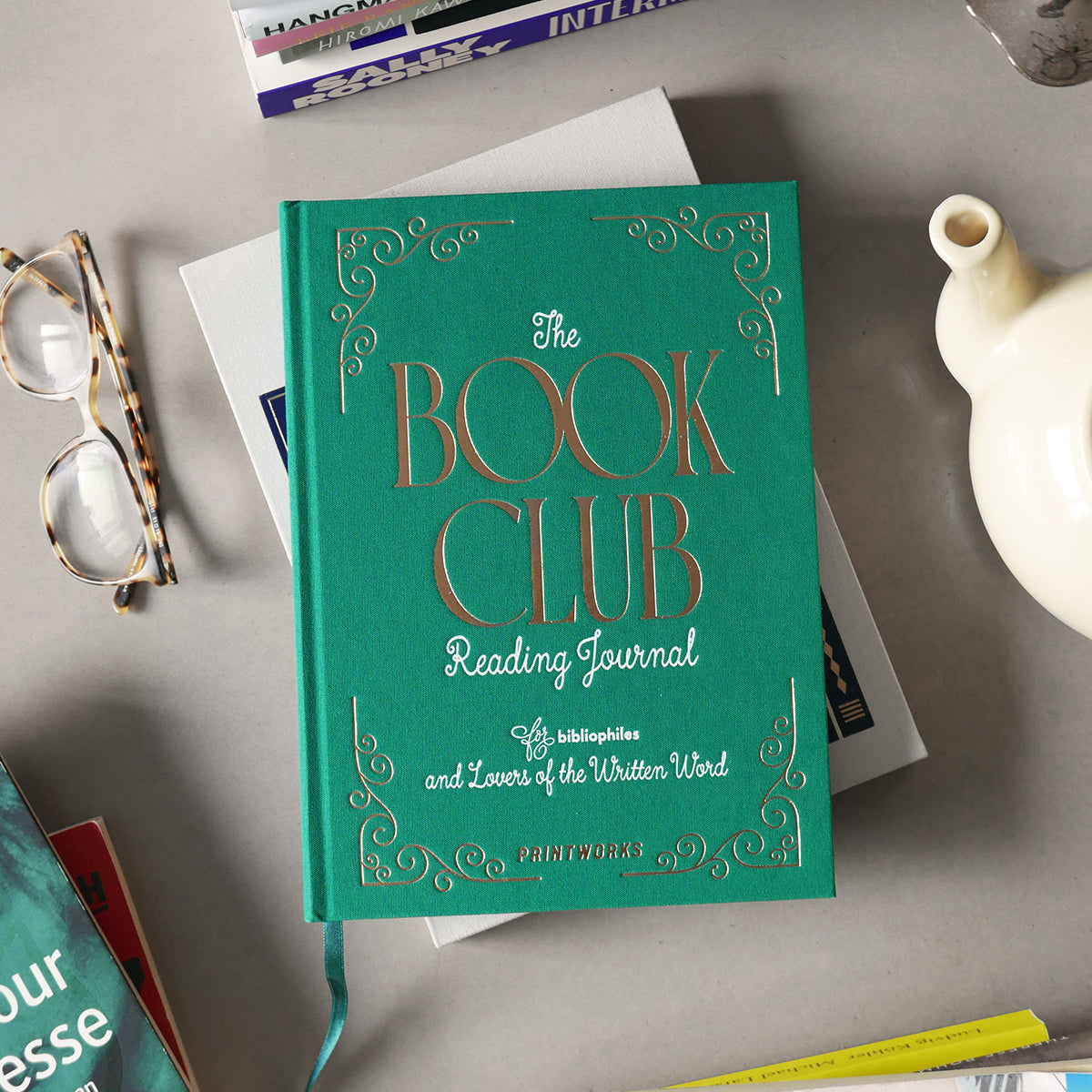 Teal book club reading journal on a surface with books and glasses around