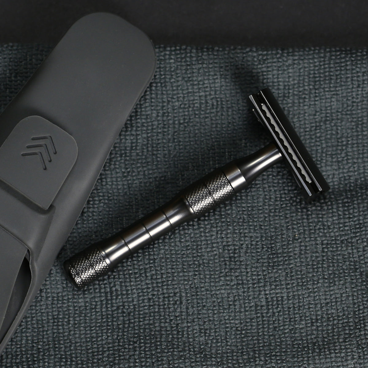 The Daily Shaver safety razor with charcoal coloured finish on a dark grey towel with the silicon razorwrap case 