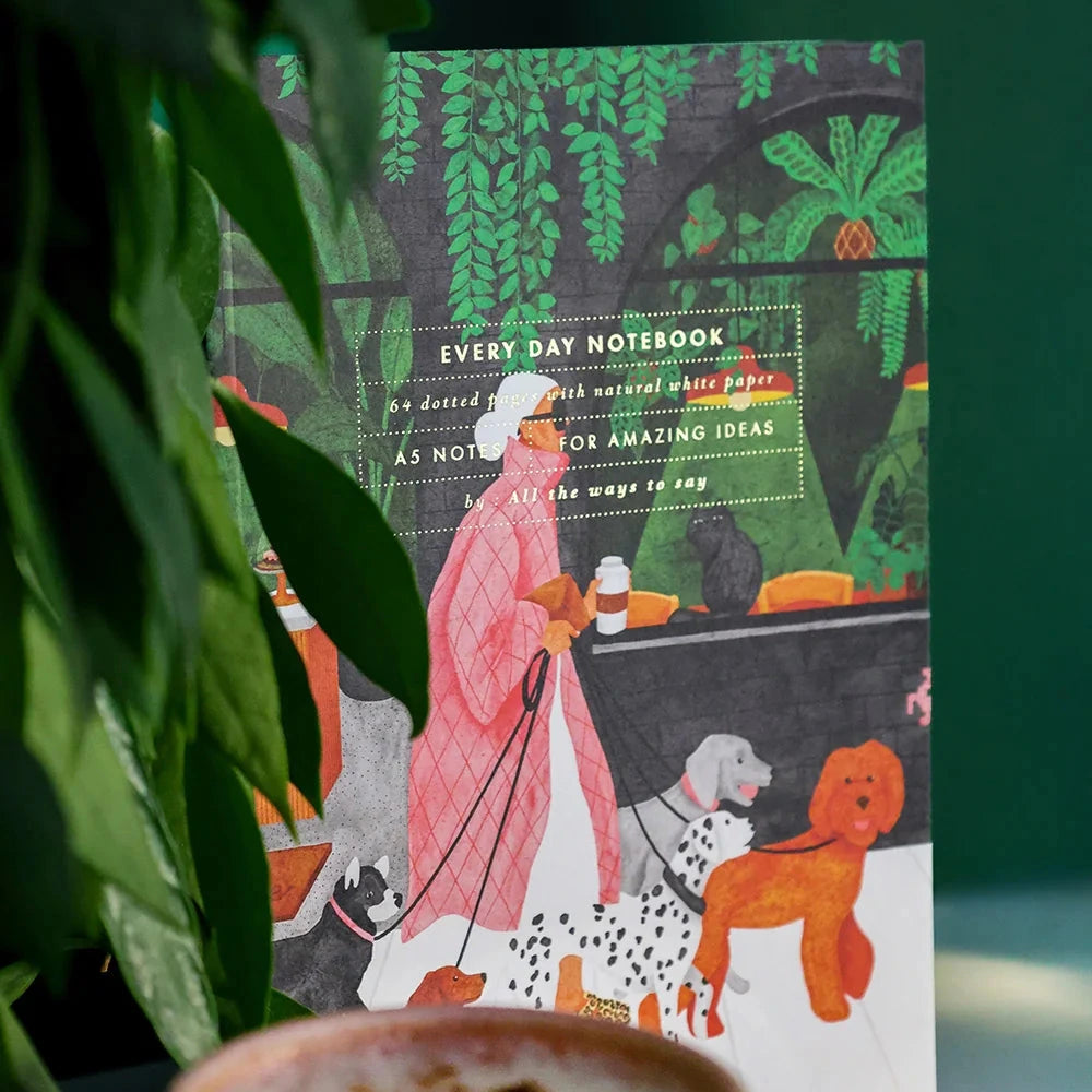Notebook with a colorful design featuring a person and dogs, placed on a surface with a blurred background.