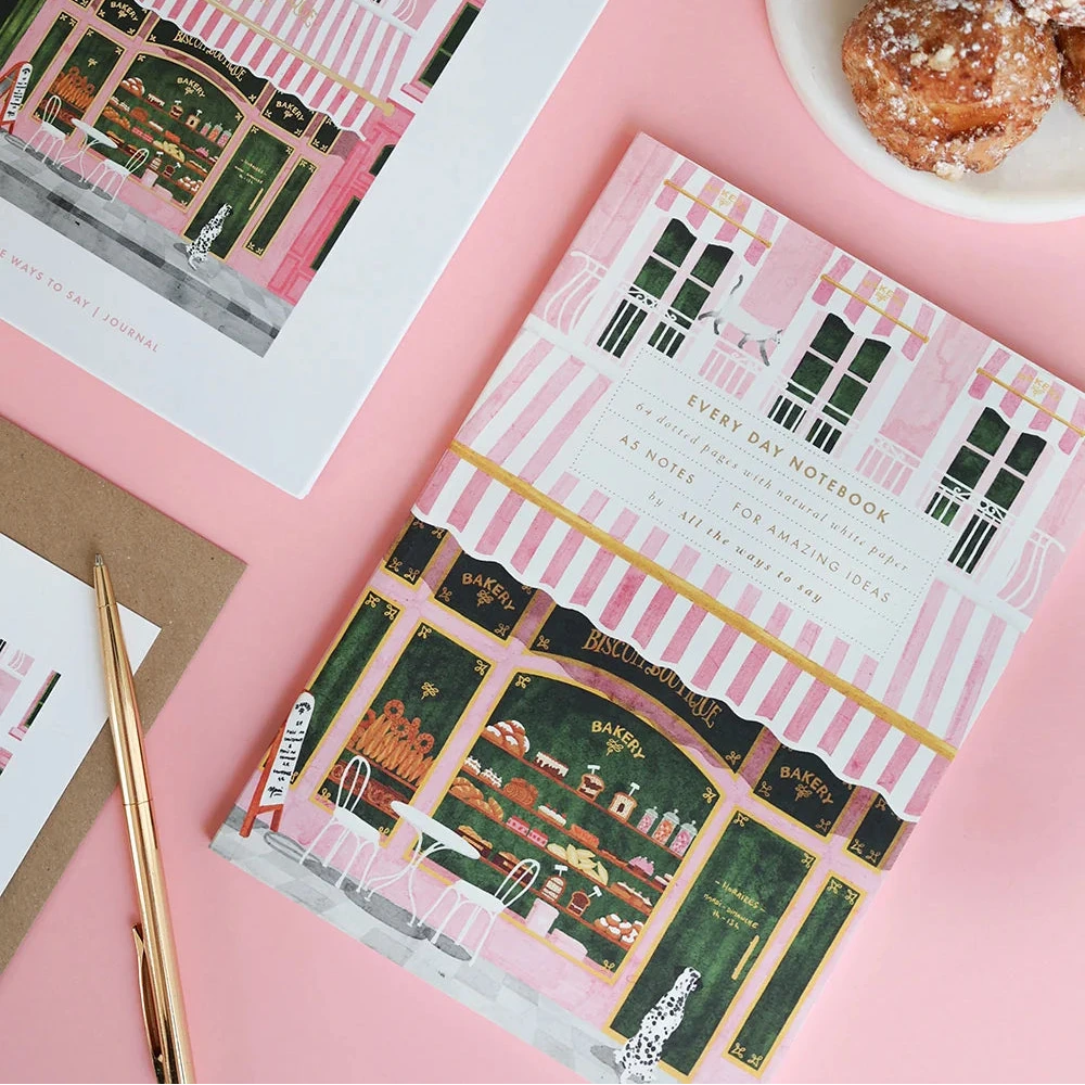 Two notebooks with decorative covers on a pink surface with pastries.