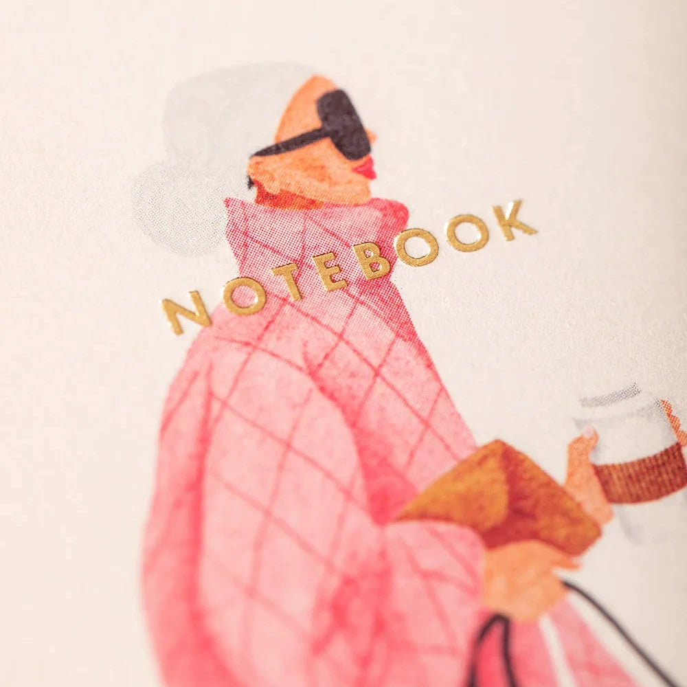 Notebook with a person in a pink outfit and goggles holding a camera on a white background