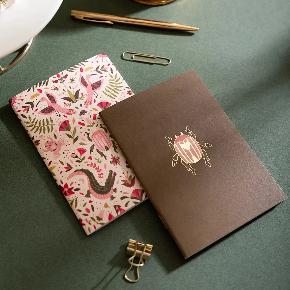 Two illustrated art cards or prints shown on a white background. The front card is olive green with a pink beetle illustration, and the back card shows a dense botanical and animal pattern in pink, green, brown, and cream.