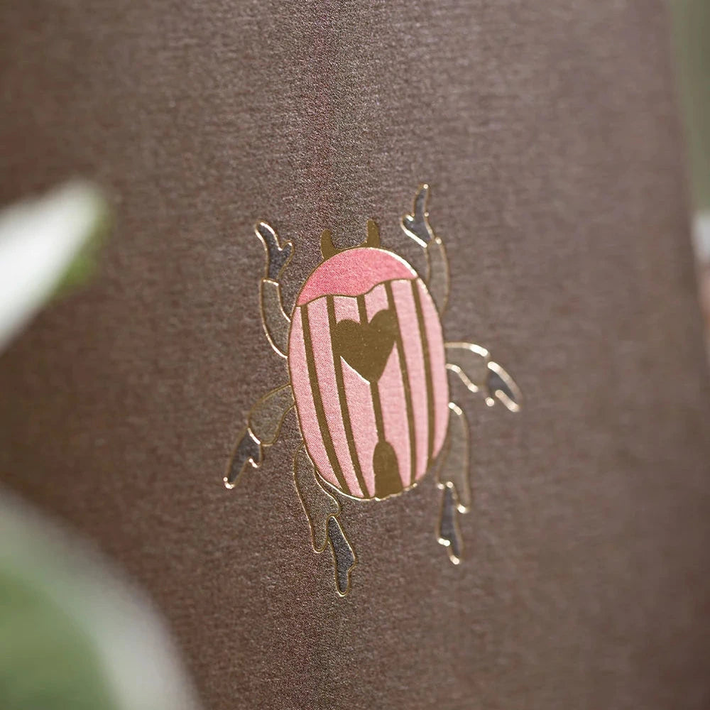A close-up of a brown textured surface featuring a small pink and gold beetle-shaped emblem with a heart design in the center.