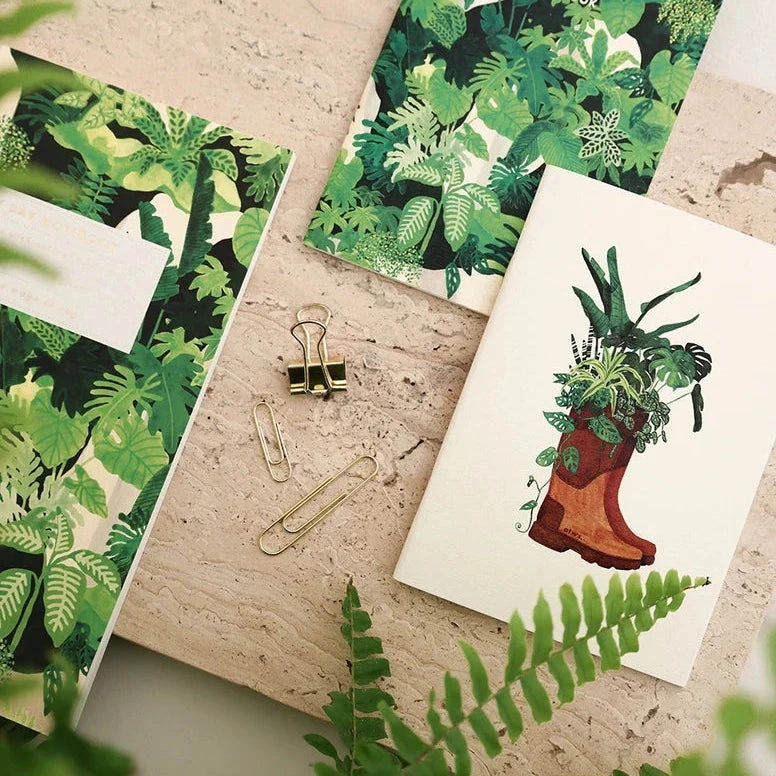 Notebooks with green leaf patterns on a wooden surface with plants around