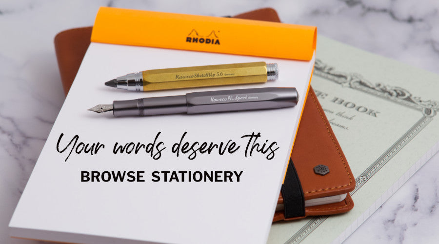 A fountain pen, a clutch pencil and a Rhodia notebook on a marble surface with a leather notebook cover