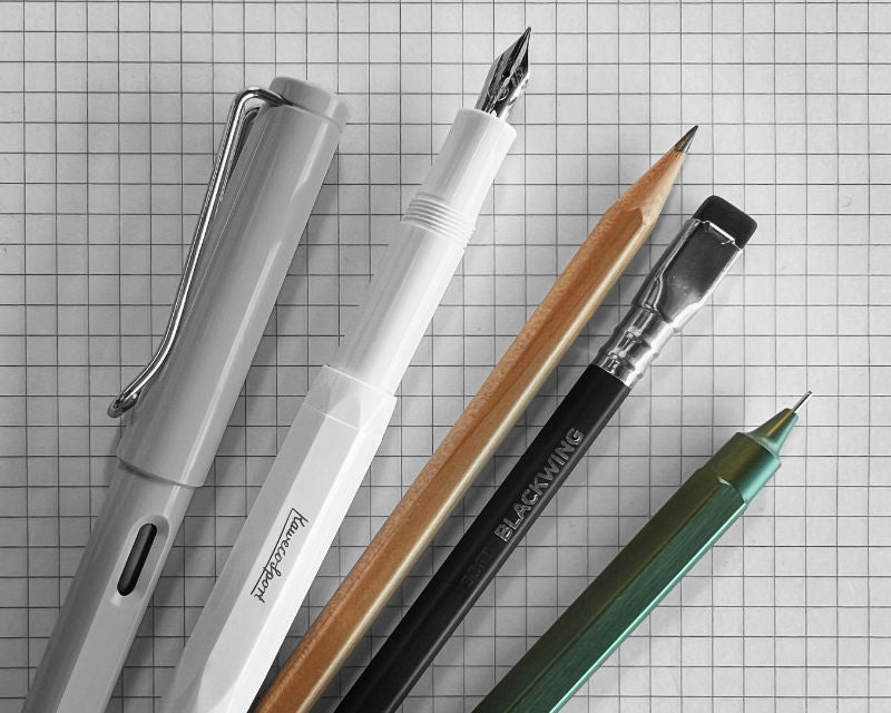 Collection of pens and pencils on a grid paper background