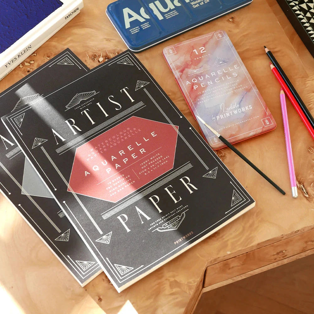 Two art supply books on a wooden table with 'Aquarelle' branding.