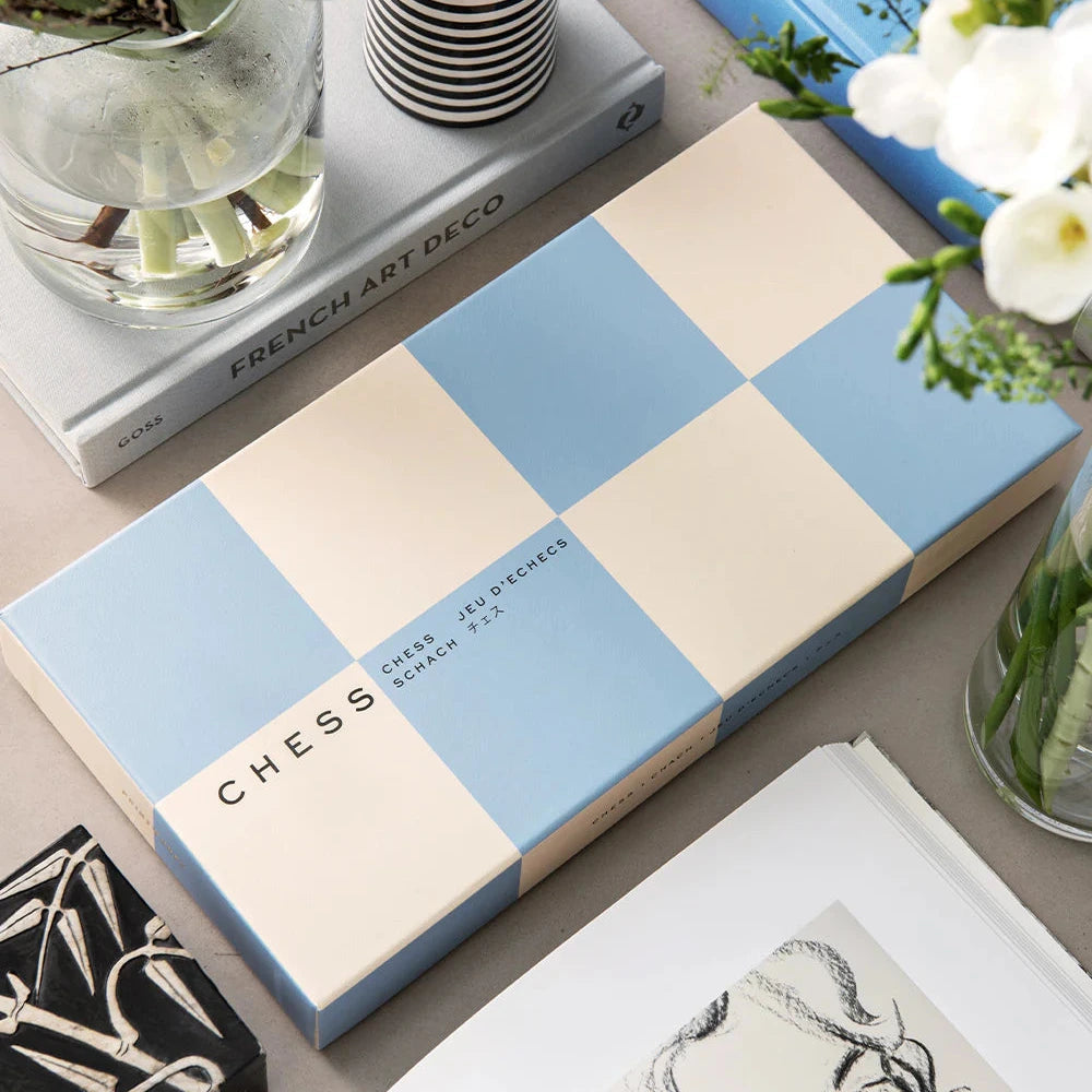 Checkered notebook with 'CHESS' branding on a surface with books and flowers.