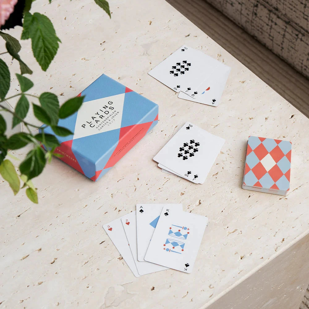 Playing cards with a geometric design box on a light surface next to a plant