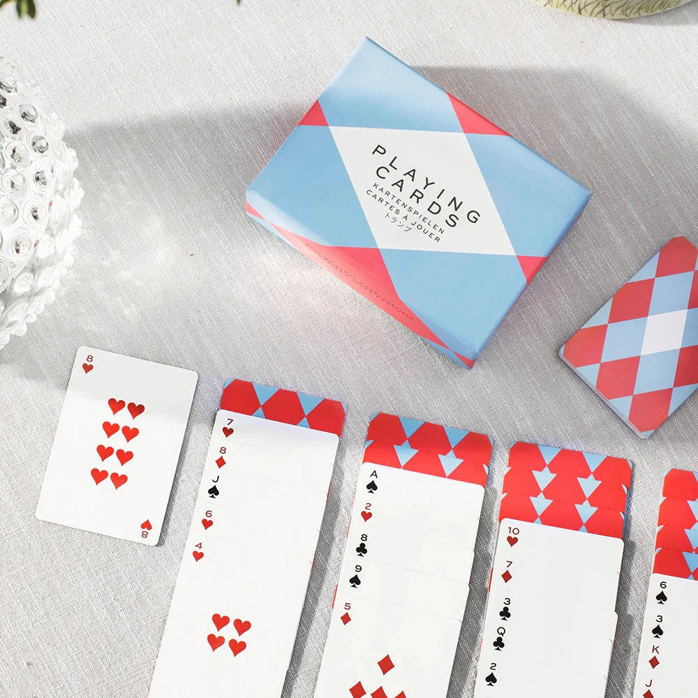 Playing cards with red and blue design on a light surface with greenery