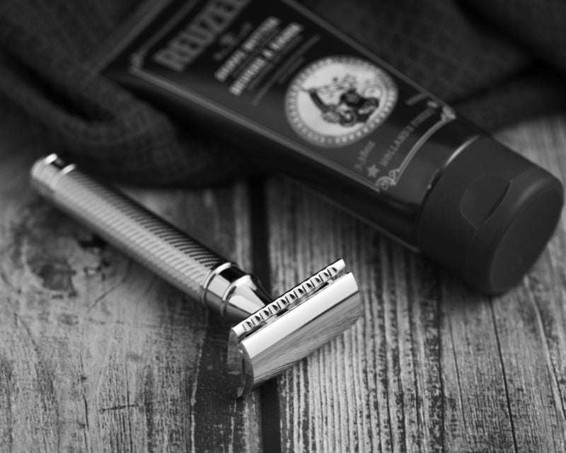 A Muhle razor and a tube of shave cream on a dark timber background with a dark waffle towel
