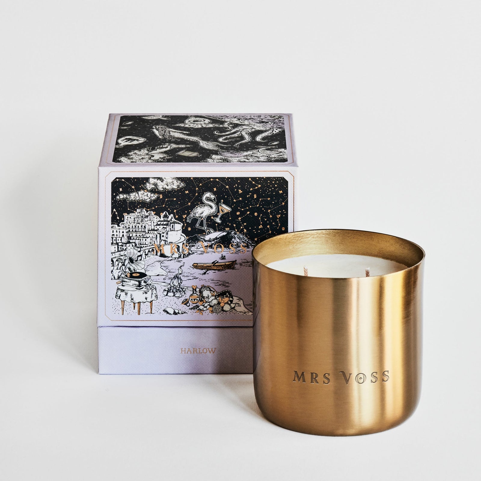 Gold candle with 'MRS VOSS' branding next to a decorative box on a light background