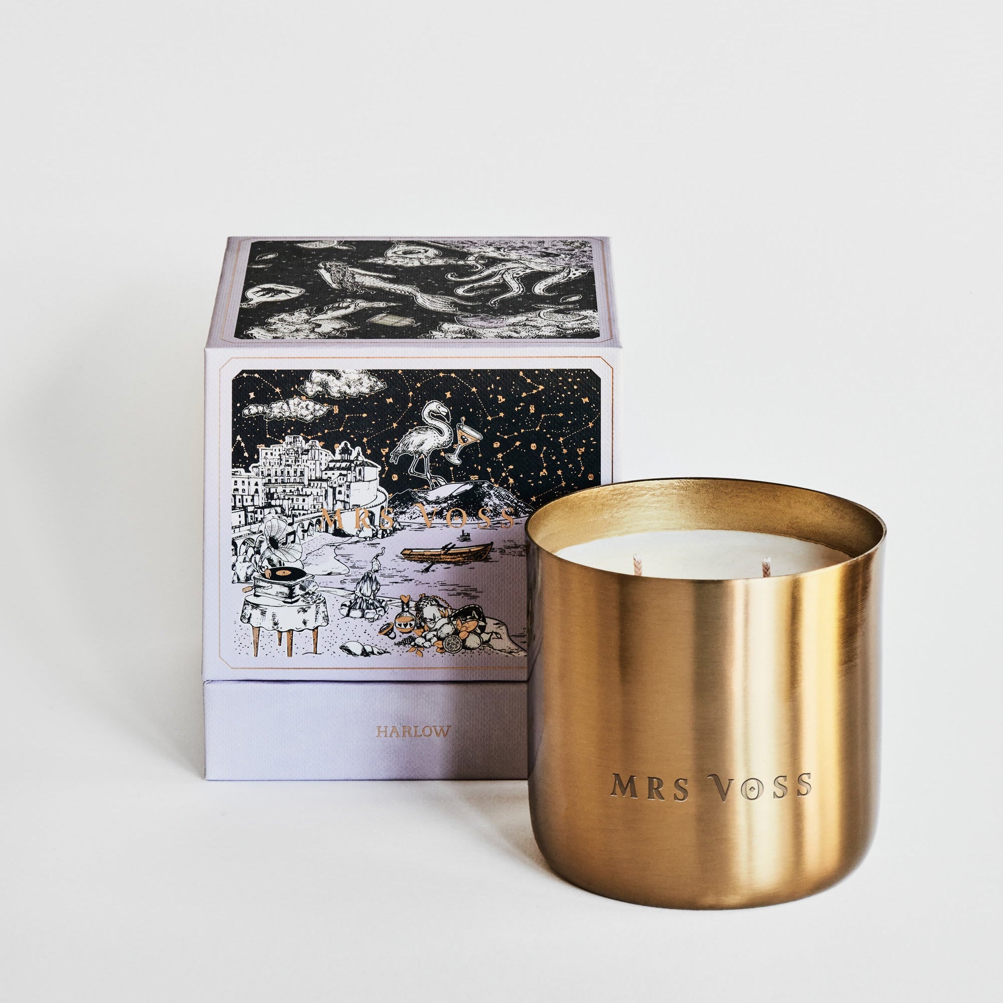 Gold candle with 'MRS VOSS' branding next to a decorative box on a light background