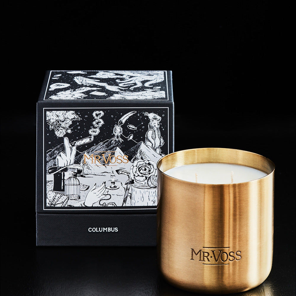 Gold candle holder with white candle and decorative box labeled 'MR. VOSS' on a light gray background