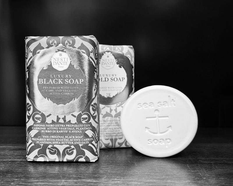 Two packages of Nesti Dante luxury black soap and a bar of Sea Salt soap on a dark surface.