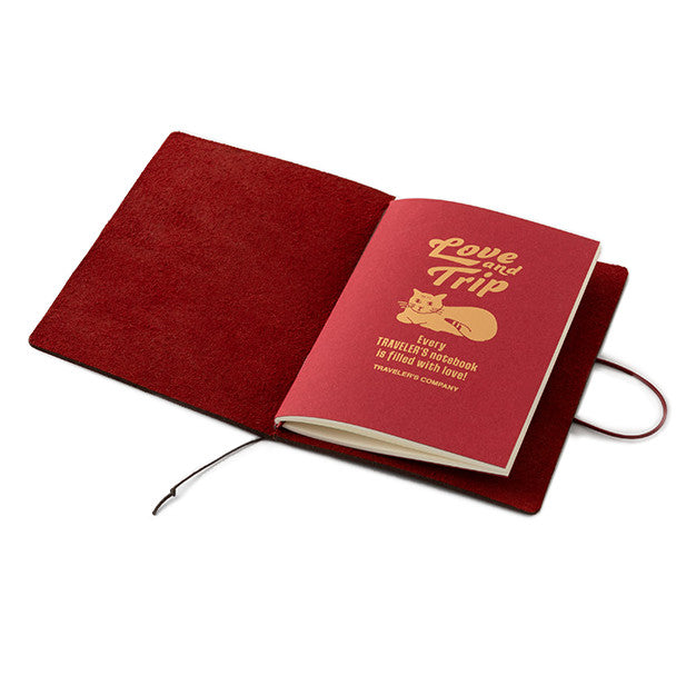 TRAVELER'S notebook passport size with a limited edition Love and Trip design, featuring a vibrant red leather cover with debossed detailing. The product also includes a cardboard packaging, a muslin slip bag, and a limited edition refill booklet with gold foil design.