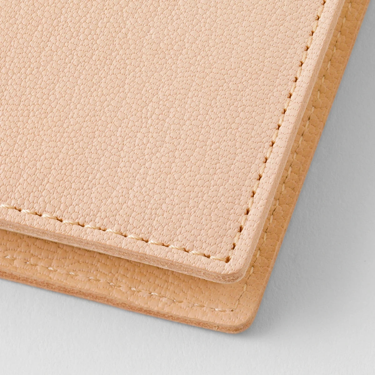 Close-up of a beige leather wallet with visible stitching on a light gray background