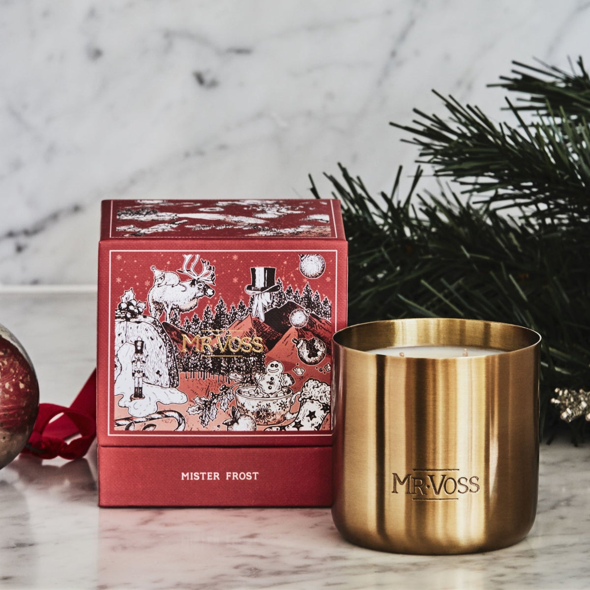 Gold candle with 'Mr. Voss' branding next to a red gift box and Christmas decorations on a marble surface.